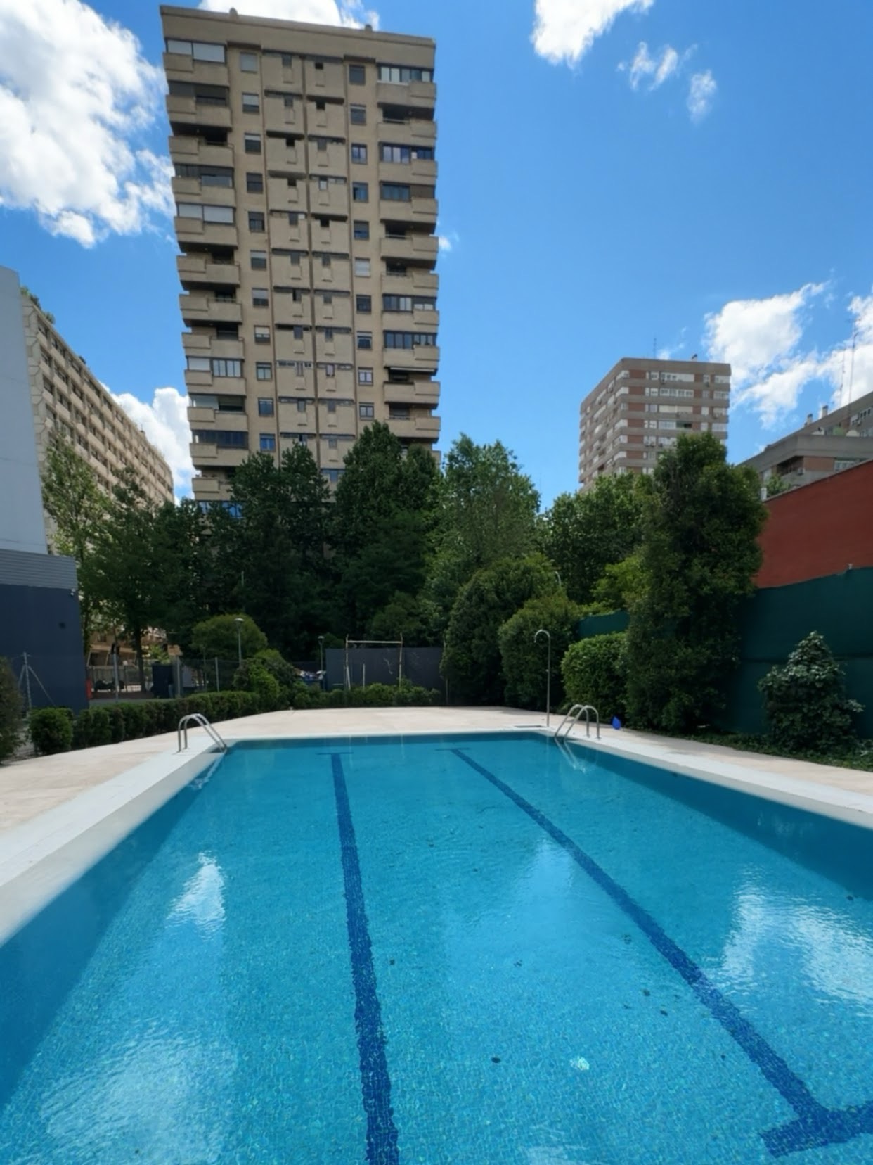 Blue outdoor community swimming pool with Madrid apartment buildings in the background, sunny day.