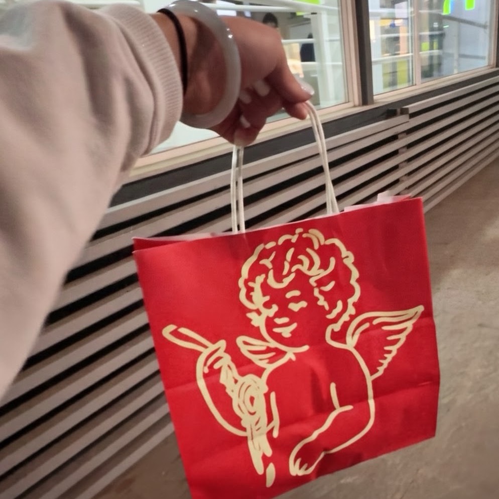 Hand holding red paper shopping bag with gold cherub angel graphic design in Madrid.