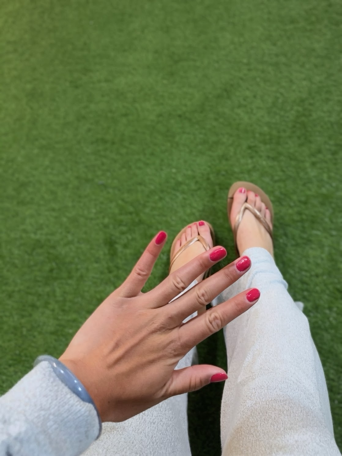 Close-up pink manicure on white linen pants with gold sandals on grass in Madrid.