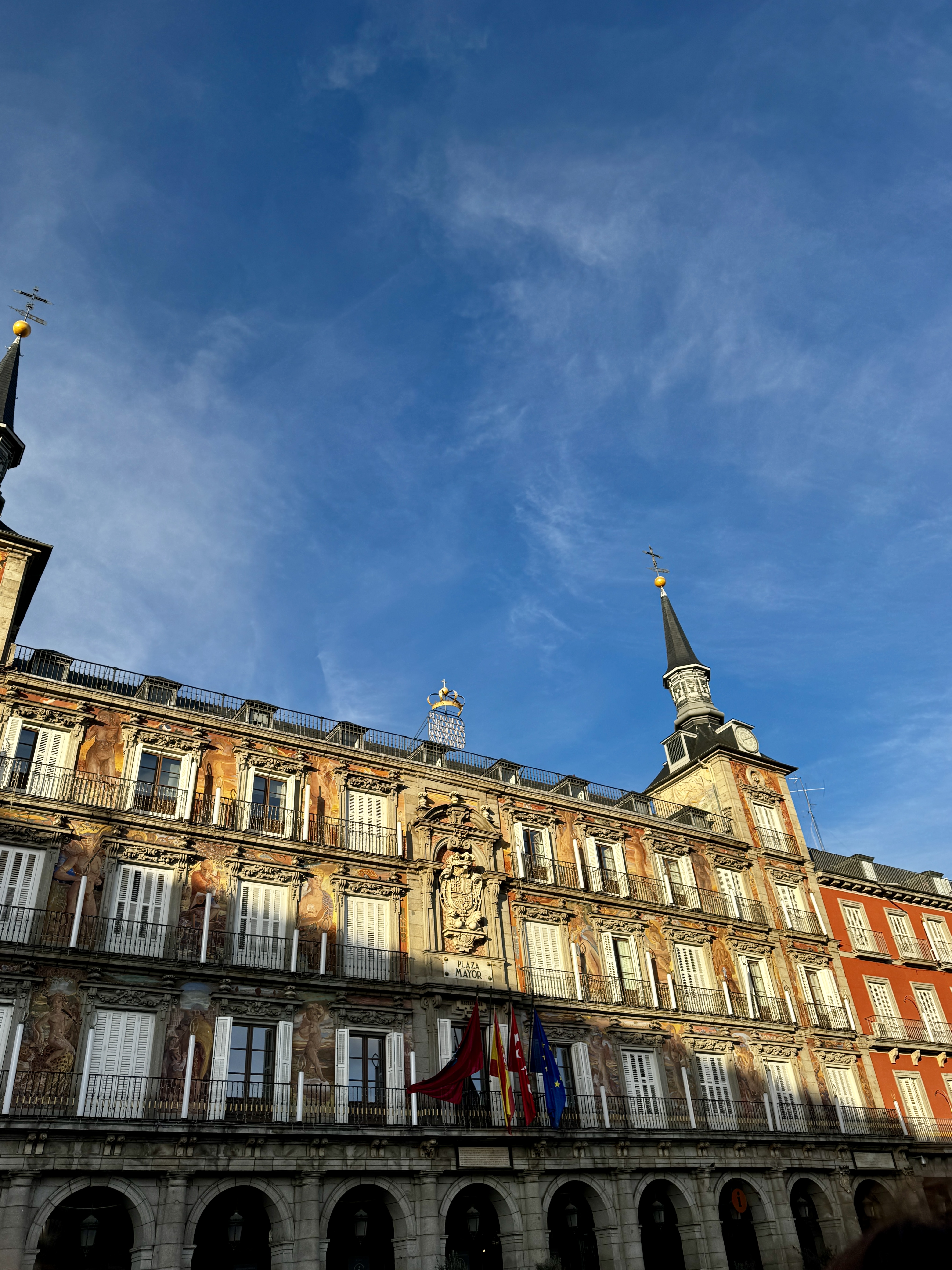 The painted frescoed facade of Casa de la Panadería at Plaza Mayor bathed in golden afternoon light, Madrid and Community flags below, Spain.