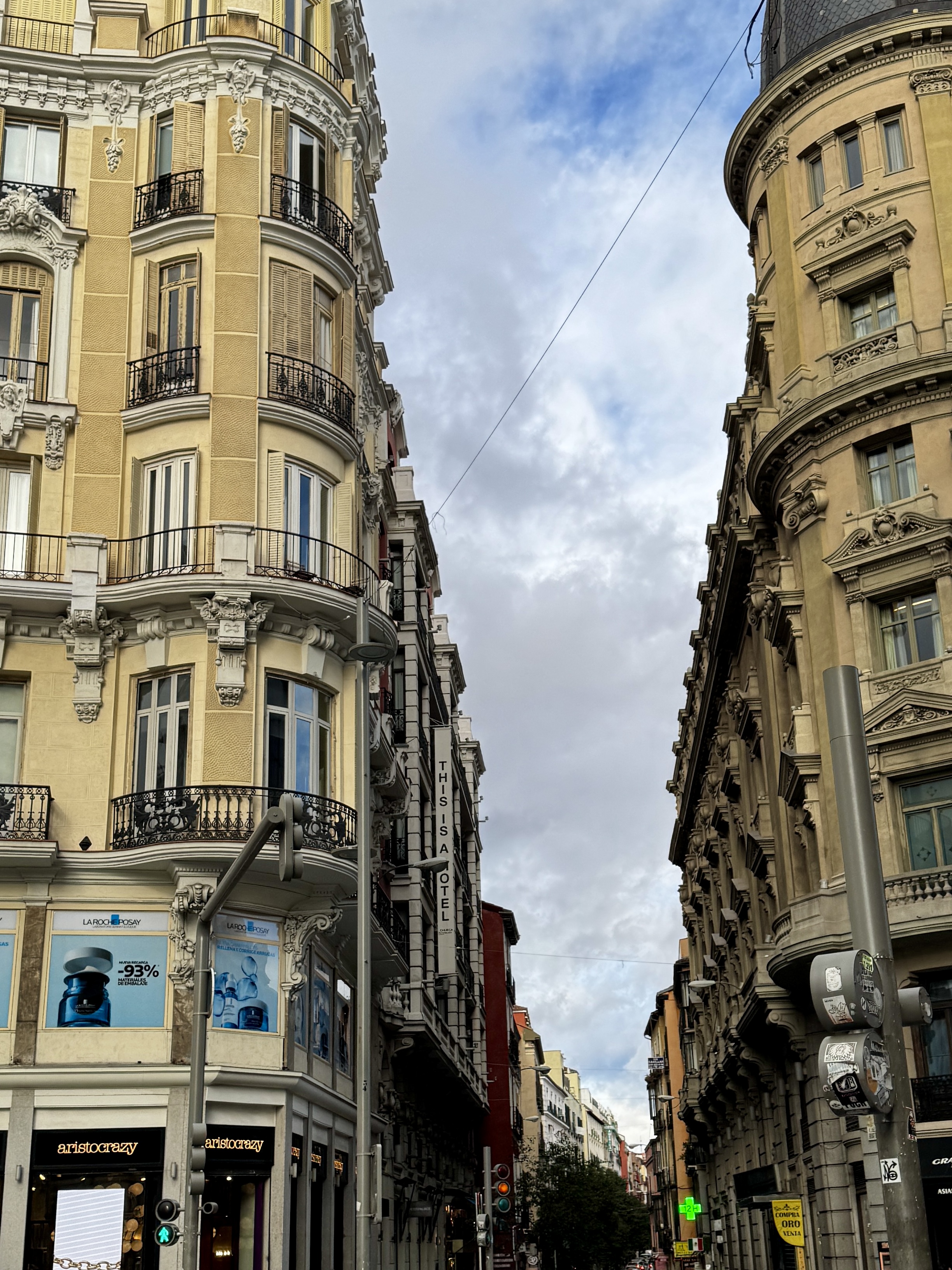 Upward view between ornate Belle Époque buildings with curved facades and iron balconies on a central Madrid street.