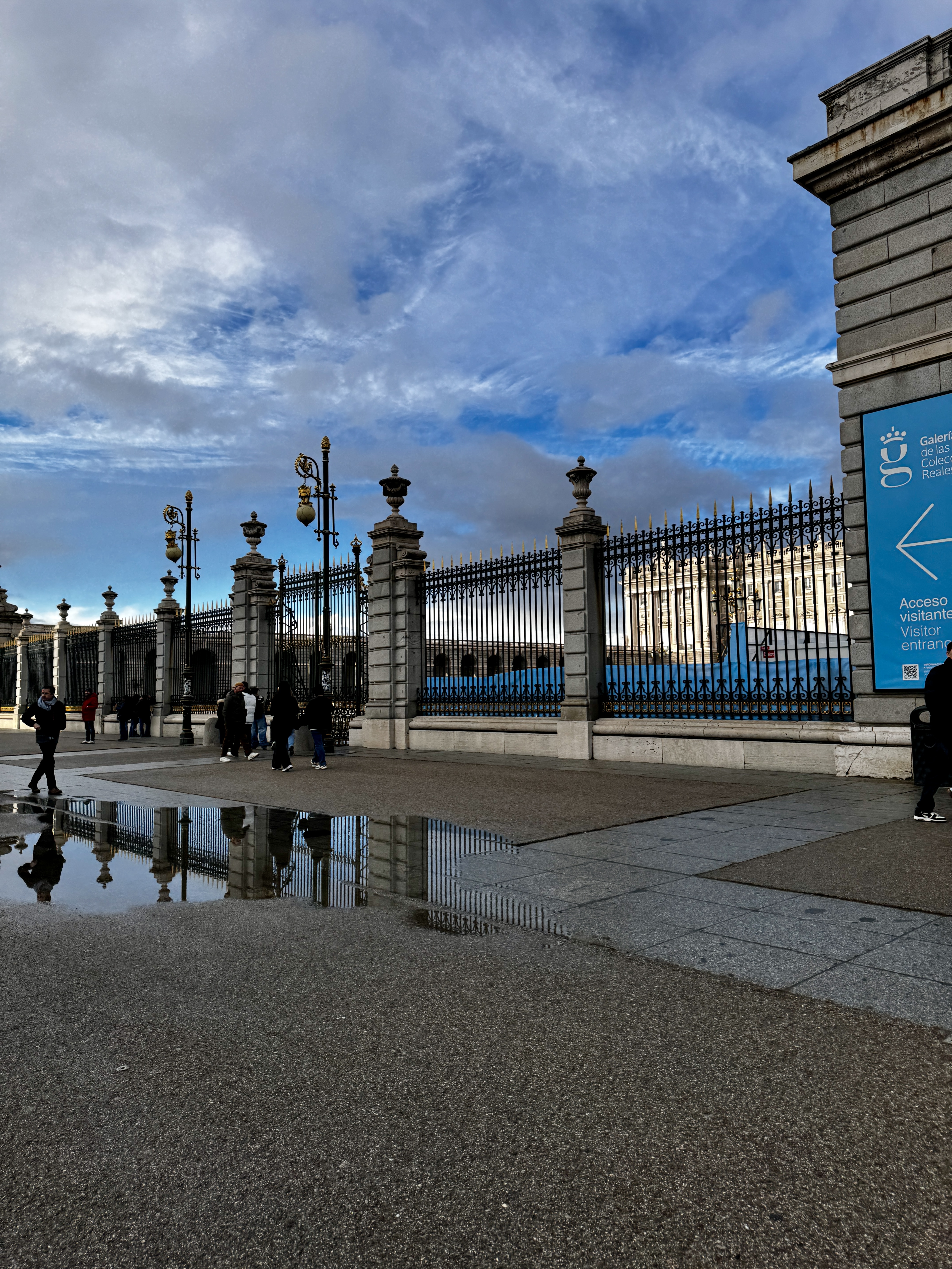 Rooftop view of a Madrid residential neighbourhood with a Spanish flag, apartment blocks, and large white clouds against a blue sky.